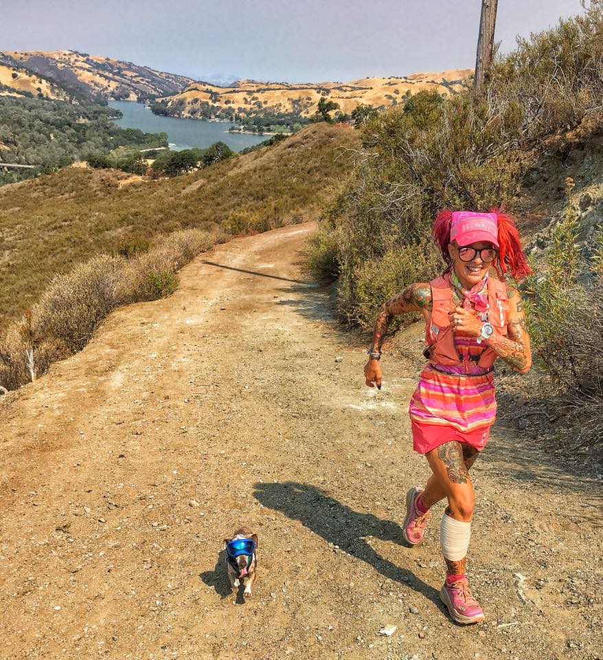 Small dog wearing Rex Specs dog goggles running with their human.