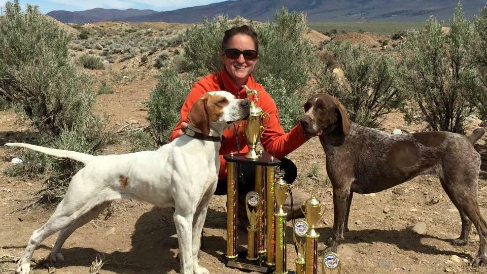 Two dogs and their handler posing outside with trophy